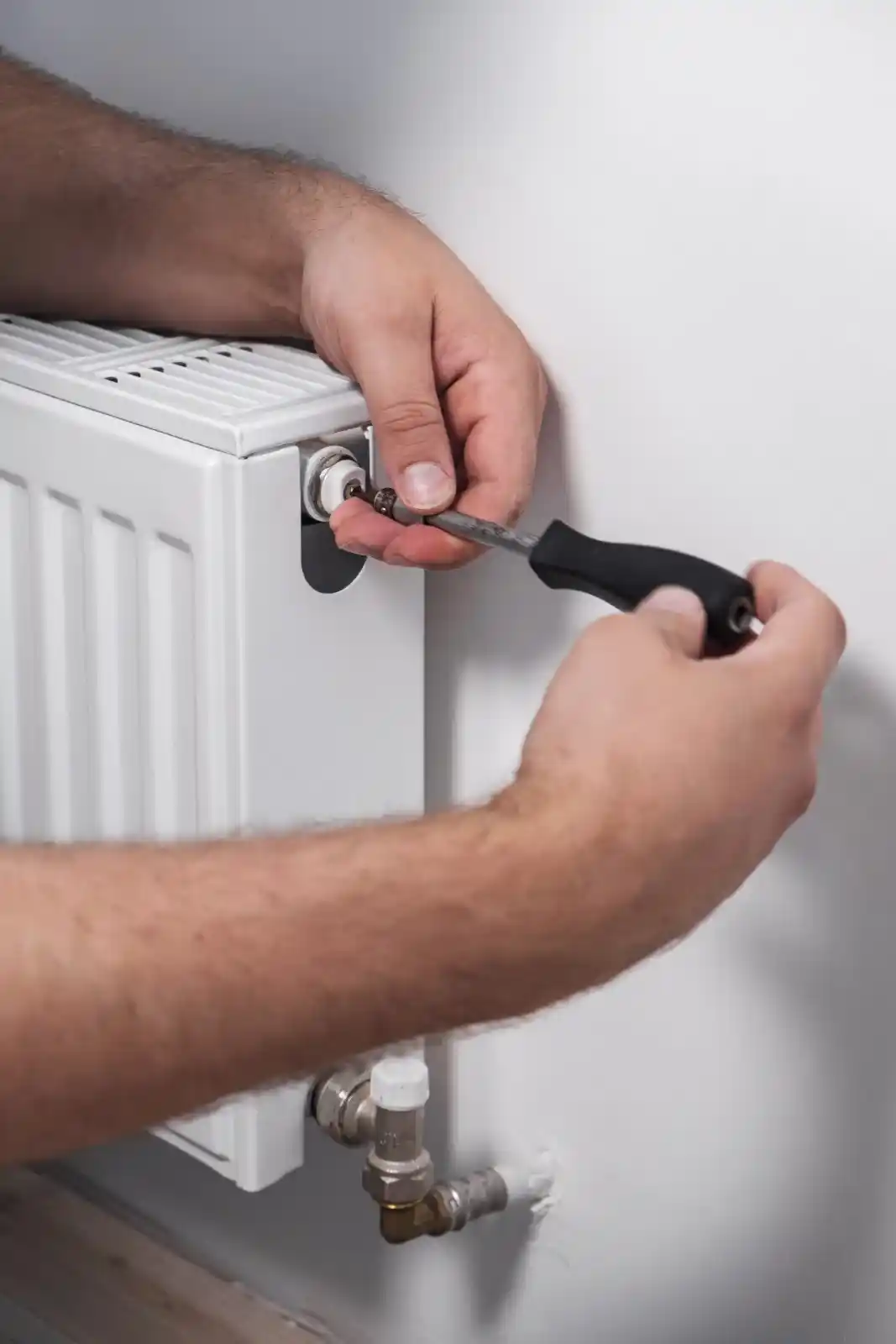 Technicien utilisant un tournevis pour réparer ou régler la vanne d'un radiateur de chauffage.